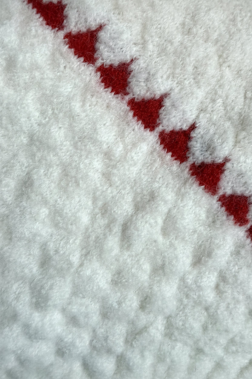 Close-up of a soft white textured fabric with a diagonal red geometric pattern.