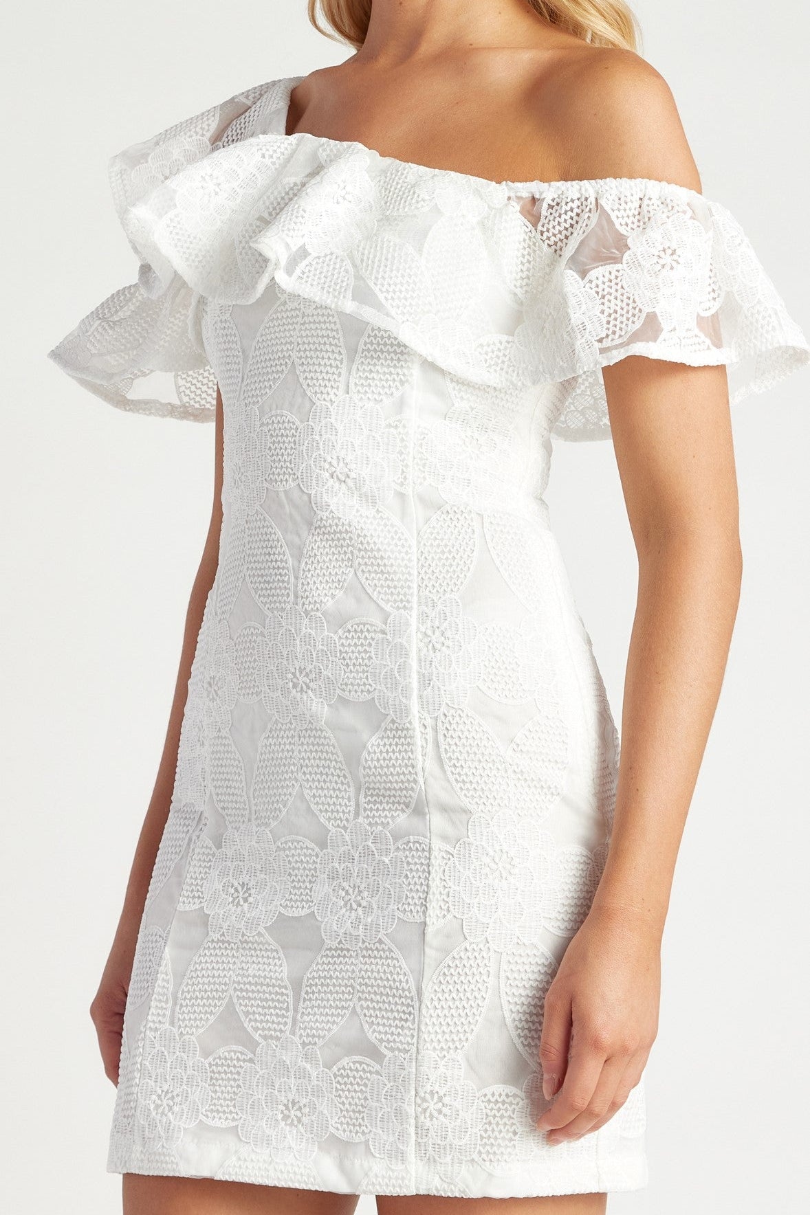 White off-the-shoulder lace mini dress with ruffled sleeves and a fitted silhouette, shown on a model against a light gray studio background.