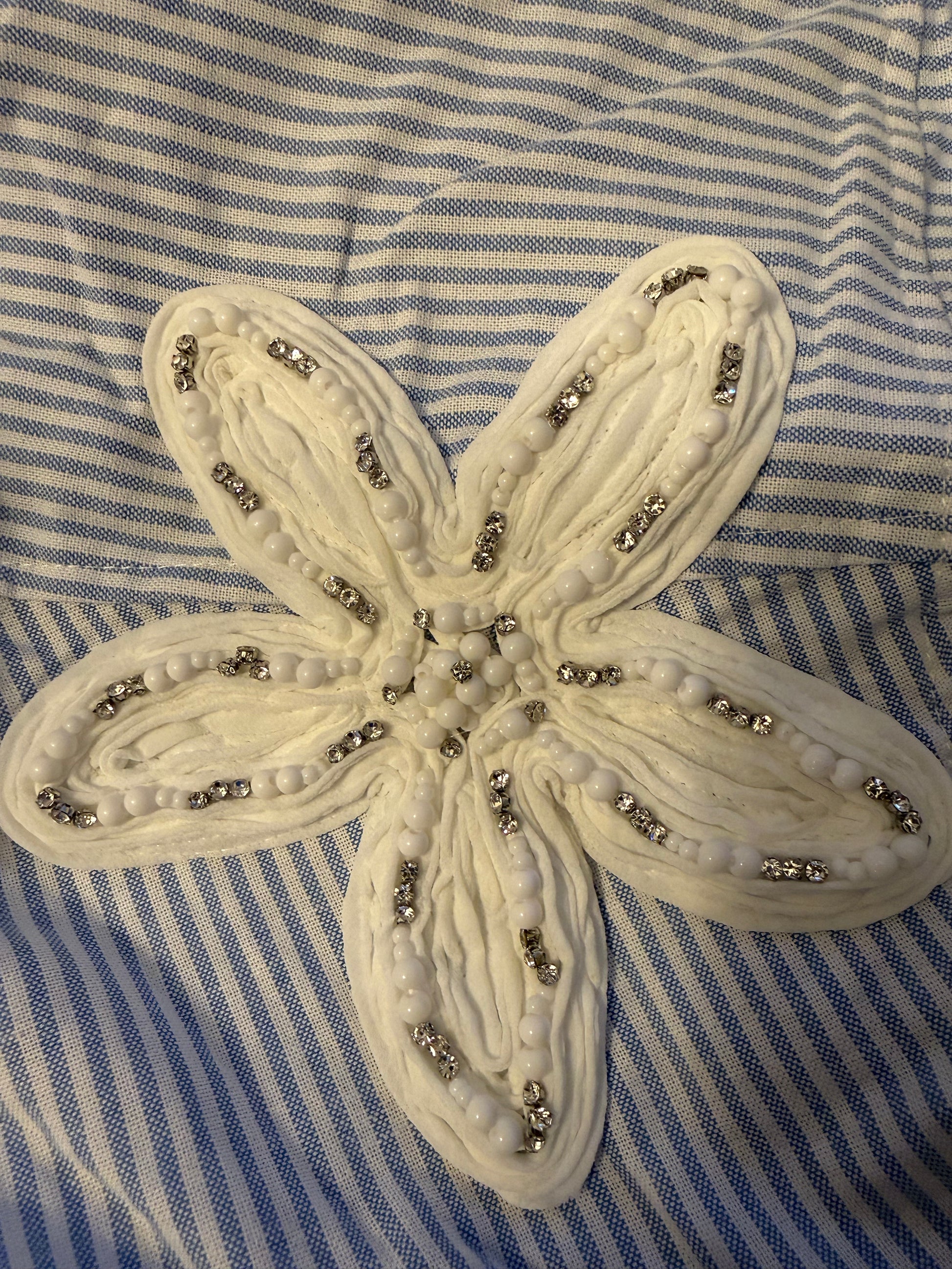 A cream-colored fabric starfish applique embellished with white beads and silver rhinestones, laid flat on a blue and white striped fabric background.