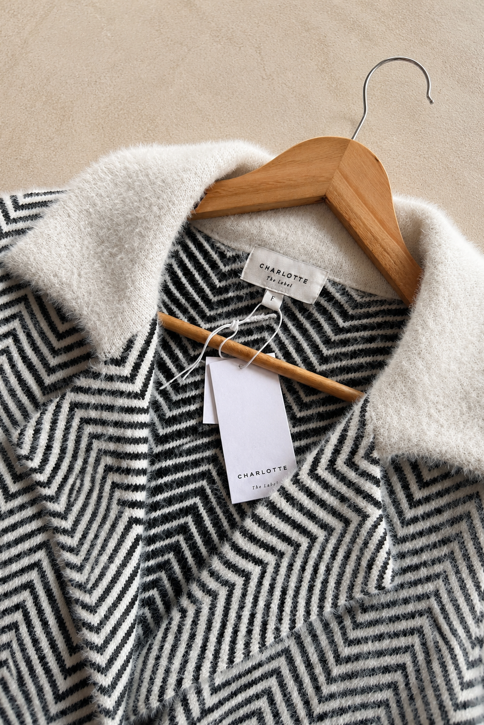Charlotte London chevron knit cardigan with a fuzzy cream collar, shown on a wooden hanger against a neutral beige background.